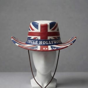 Könnte beinhalten: Ein breitkrempiger Hut mit einem rot-weiß-blauen Union-Jack-Flaggenmuster. Ein dunkelblaues Band umschließt die Krone, auf dem vorne der weiße Schriftzug "UNCLE HOLLYWOOD" aufgedruckt ist. Der Hut verfügt über einen dünnen braunen Kinnriemen.