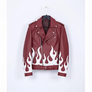Peut inclure: Veste en similicuir bordeaux avec une fermeture éclair asymétrique classique. Des flammes blanches ornent les manches et le bas de l'avant. Col à revers, ceinture à la taille et fermetures éclair argentées.