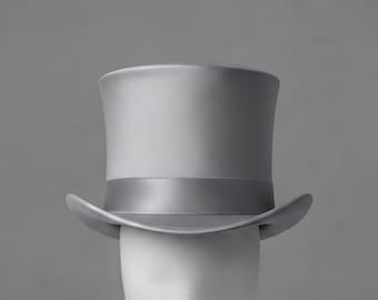 May include: A solid light gray top hat featuring a smooth, matte finish and a matching gray satin ribbon band encircling the base of the crown. The hat has a structured, cylindrical crown and a curved brim that turns upward at the sides.