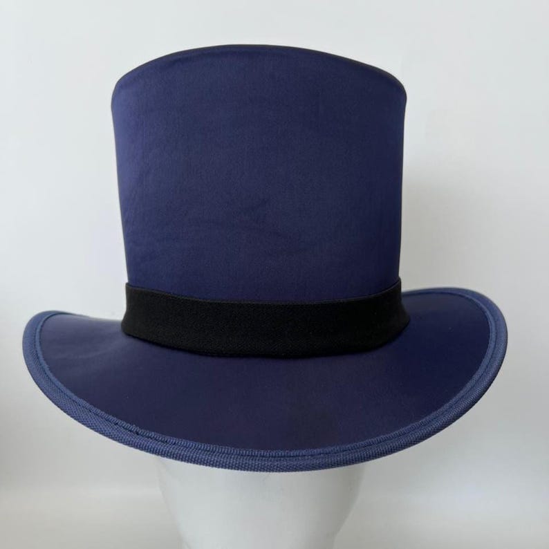 Puede incluir: Un sombrero de copa azul marino con una banda negra. El sombrero tiene un ala ancha y una copa cil&iacute;ndrica alta. El sombrero se exhibe sobre una cabeza de maniqu&iacute; blanca.