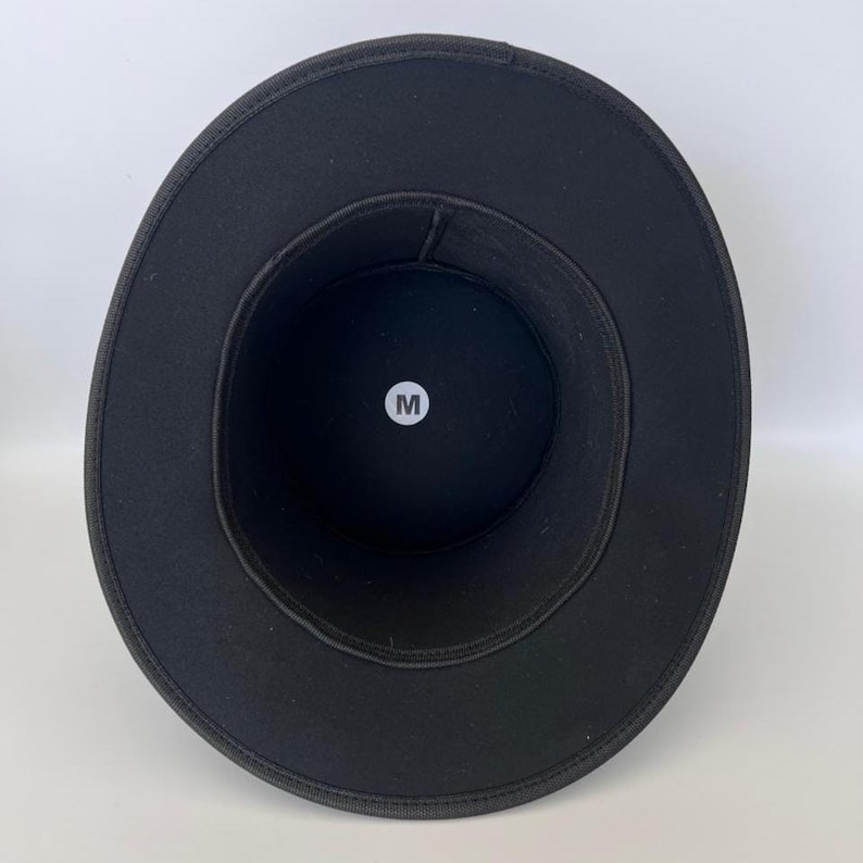 Puede incluir: Un sombrero negro con ala ancha, visto desde el interior. El sombrero tiene forma circular con un ala de tama&ntilde;o mediano. Una etiqueta circular blanca con la letra "M" es visible en el interior.