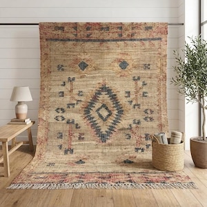Peut inclure: Un tapis rectangulaire en fibres naturelles de couleur beige, orné d'un motif central en losange bleu foncé. Le tapis présente des motifs géométriques rouges et bleus, des bandes horizontales et une bordure à franges sur le bas du textile.