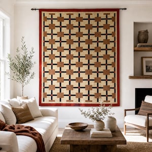 K&ouml;nnte beinhalten: Ein rechteckiger Wandbehang mit einem geometrischen Gittermuster aus beigen Quadraten, die durch d&uuml;nne schwarze vertikale und horizontale Linien getrennt sind, akzentuiert durch kleine rote Quadrate an den Schnittpunkten, umrandet von einem roten Rand.