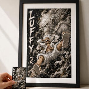Peut inclure: Impression d'art encadrée noire représentant une illustration dynamique d'un personnage avec le mot "LUFFY" verticalement à gauche. L'œuvre d'art représente une figure en mouvement et une grande créature. Une petite carte avec la même image est tenue à proximité.