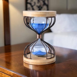 Könnte beinhalten: Sanduhr mit blauem Sand, umhüllt von einem Metallkäfig mit Holzober- und -unterseite. Die Sanduhr steht auf einer dunklen Holzoberfläche. Das Design zeichnet sich durch eine klassische Form mit moderner Ästhetik aus.