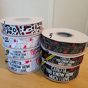 May include: Five spools of black and white ribbon with red accents. The ribbon has a crime scene tape design with the text "True Crime" and "Careful... You Know How Much I Love".