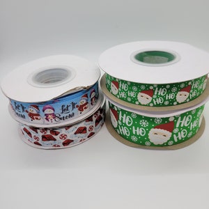 May include: Three spools of Christmas ribbon. The first spool has a blue background with white snowmen and the text "Let it Snow". The second spool has a white background with red candy canes and the text "Ho Ho Ho". The third spool has a green background with white snowflakes and the text "Ho Ho Ho" with a Santa Claus face.