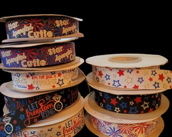 May include: A stack of spools of red, white, and blue ribbon with patriotic designs. The ribbons feature text such as "Star Spangled Cutie", "Let Freedom Ring", and "I'm not just a Princess, I'm a Veteran's Princess".