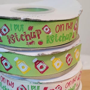 May include: A stack of four rolls of green, white, and yellow ribbon with a ketchup bottle and the text "I put ketchup on my ketchup" printed on them.