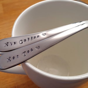 Pu&ograve; includere: Due cucchiai d'argento con cuori incisi e il testo "His Coffee" e "Her Tea" su una tazza bianca.