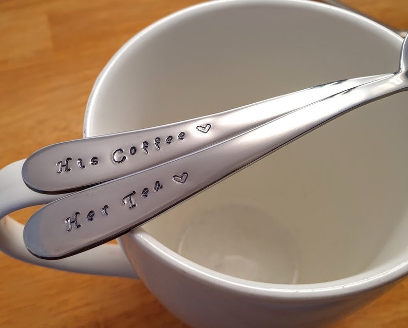 Pu&ograve; includere: Due cucchiai d'argento con cuori incisi e il testo "His Coffee" e "Her Tea" su una tazza bianca.