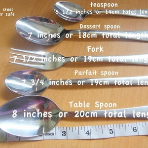 May include: A set of five stainless steel utensils, including a teaspoon, dessert spoon, fork, parfait spoon, and table spoon. The utensils are laid out in order of size, with the teaspoon at the top and the table spoon at the bottom. The utensils are all dishwasher safe. The text on the image reads: "stainless steel dishwasher safe", "teaspoon 5 1/2 inches or 14cm total length", "Dessert spoon 7 inches or 18cm total length", "Fork 7 1/2 inches or 19cm total length", "Parfait spoon 7 3/4 inches or 19cm total length", "Table Spoon 8 inches or 20cm total length".