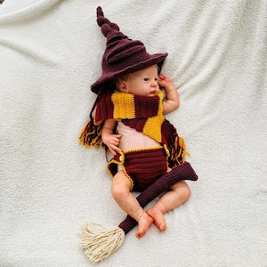 Peut inclure: Un bébé portant un costume de sorcier au crochet bordeaux et or, comprenant un chapeau pointu, une écharpe, une culotte et un balai. Le costume est posé sur une couverture blanche. L'écharpe a des rayures jaunes et bordeaux.