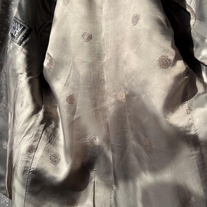 May include: Interior view of a gray blazer with a silky lining. The lining is patterned with small, repeating floral designs. A label with the text "Gianni Versace" is visible on the inside.