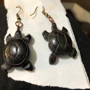 May include: A pair of black turtle earrings with a carved design. The earrings are made of a dark, polished material and have a simple, elegant design.