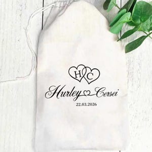 Puede incluir: Una bolsa blanca con cordón y texto negro y gráficos de corazón. El texto incluye los nombres "Hurley" y "Cersei", las iniciales "H C" dentro de corazones y la fecha "22.03.2026".
