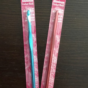May include: Two Susan Bates aluminum crochet hooks, one blue and one red, packaged in pink and white wrappers. The hooks are labeled with their sizes: 5 mm (H8 US) and 5.5 mm (I9 US).