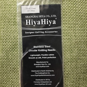 May include: A silver circular knitting needle with a black label that reads "Stainless Steel Circular Knitting Needle" and includes information about the manufacturer and distributor. The label also states "Lightweight, Flexible cables Smooth as silk, Point perfection". The needle is 12 inches or 30 centimeters long and is size US 9/5.5mm.