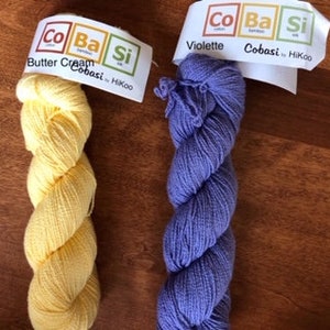 May include: Two skeins of yarn, one in a pale yellow color called "Butter Cream" and the other in a light purple color called "Violette". Both skeins are labeled "CoBaSi" by HiKoo.