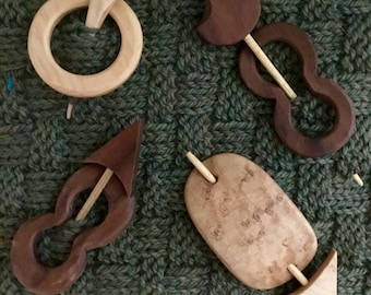 May include: Four wooden knitting stitch markers with different shapes and designs. Two are brown and two are natural wood.