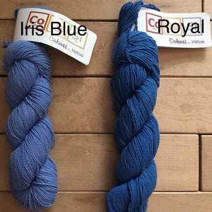May include: Two skeins of Cobasi yarn by HiKoo in blue shades. The skein on the left is labeled "Iris Blue" and the skein on the right is labeled "Royal".