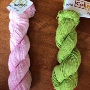 May include: Two skeins of yarn, one pink and one green. The pink skein is labeled "Bubblegum" and the green skein is labeled "Kiwi".
