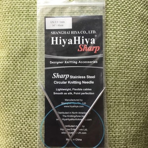 May include: A close-up of a HiyaHiya Sharp circular knitting needle in a clear plastic package. The needle is 16 inches long and is made of stainless steel. The package also includes information about the manufacturer and distributor.
