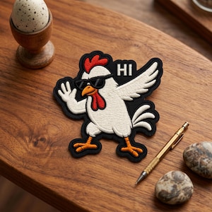 May include: Embroidered patch featuring a white chicken wearing sunglasses and waving, with the word "HI" above it. The patch has a black border and orange feet. The image is on a wooden surface.