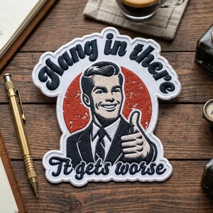 May include: Embroidered patch with a retro design featuring a man giving a thumbs-up. The patch has the words "Hang in there" and "It gets worse" in a vintage font. The background is a red circle.