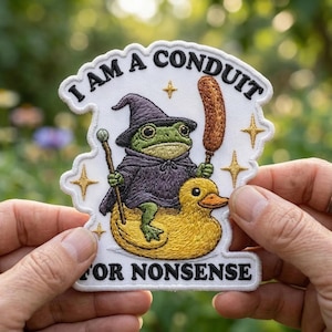 May include: Embroidered patch featuring a green frog in a wizard hat and cloak riding a yellow duck. The patch reads "I AM A CONDUIT FOR NONSENSE" in white text. The patch has a white border and gold star accents.