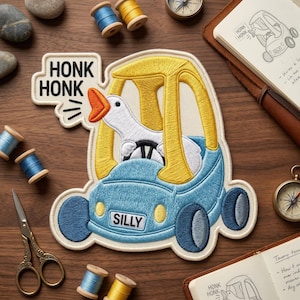 May include: Embroidered patch featuring a goose driving a blue car with yellow accents. The patch reads "HONK HONK" and "SILLY". The goose is honking. The patch is surrounded by sewing supplies and a compass.
