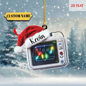 May include: A white medical monitor Christmas ornament with a red Santa hat and the name "Kevin". The monitor displays a waveform and colorful lights. The ornament has the text "CUSTOM NAME" and "2D FLAT".