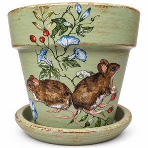 May include: A sage green terracotta plant pot with a matching saucer, featuring hand-painted illustrations of two brown mice, blue morning glory flowers, and red berries on a vine. The pot has a distressed finish along the rim and base.
