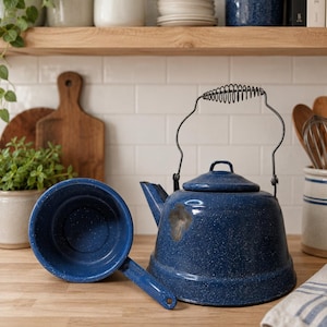 May include: A blue speckled enamel tea kettle with a wire coil handle and a matching blue speckled enamel saucepan with a long handle. The kettle features a small area of surface wear on the side, and both items have a glossy, mottled finish.