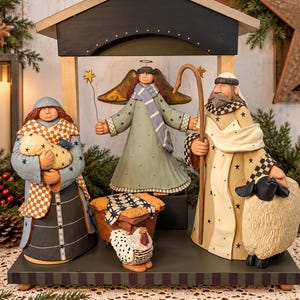 May include: A nativity scene figurine set featuring a central wooden stable structure. Figures include a person holding a swaddled infant, an angel with gold wings, and a shepherd with a staff and a sheep. A small manger and a chicken are included.