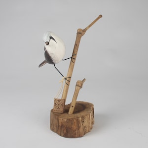 Könnte beinhalten: Eine handgefertigte Holzskulptur eines Vogels mit weißem und schwarzem Körper, der auf einem Bambuszweig sitzt. Der Vogel steht auf einem Holzsockel mit einem kleinen, quadratischen Schild mit der Aufschrift "Archipelago". Die Skulptur ist ein einzigartiges Kunstwerk.