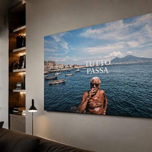 May include: A rectangular wall art print featuring a photograph of a shirtless person with sunglasses smoking a cigarette by the sea, with small boats, a distant mountain, and the white text TUTTO PASSA overlaid on the blue water and sky.