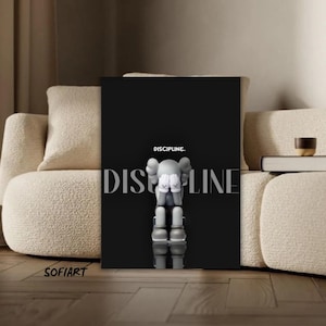 May include: A black canvas art print featuring a grey figure with white gloves and a cross design on its feet. The word "DISCIPLINE" is above the figure, with "DISCIPLINE" written vertically. The artwork is displayed in a modern living room setting.