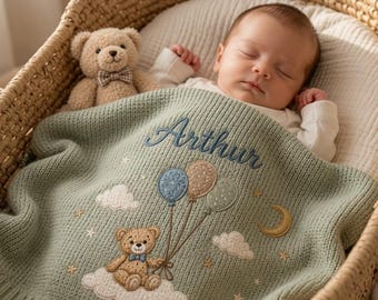 Può includere: Una coperta per neonati in maglia verde salvia con un orsacchiotto ricamato che tiene tre palloncini, nuvole bianche, stelle e una mezzaluna. Il nome Arthur è ricamato in corsivo blu scuro sopra l'orso. Un piccolo orsacchiotto di peluche è vicino.