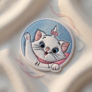 May include: Embroidered patch featuring a white cat with blue eyes, pink ears, and a pink bow. The cat is set against a light blue background within a circular frame. The patch is detailed with black whiskers and a pink scarf.