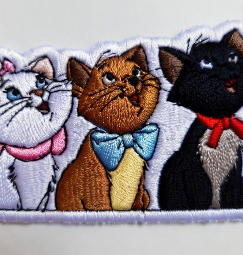 May include: Embroidered patch featuring three cartoon cats. The cats are white, brown, and black, each with unique expressions and accessories. The white cat wears a pink bow, the brown cat a blue bow tie, and the black cat a red bow.