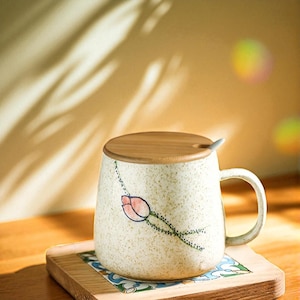 Peut inclure: Mug en c&eacute;ramique cr&egrave;me avec un motif floral, un couvercle en bois et une petite cuill&egrave;re. La tasse pr&eacute;sente une illustration de tulipe rose et rouge avec des tiges vertes. Elle repose sur un dessous de verre en bois avec un motif color&eacute;.