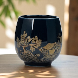 May include: A dark blue ceramic cup with a gold landscape design featuring trees and buildings. The cup has a rounded shape and a glossy finish, suitable for beverages.
