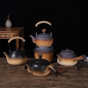 May include: A collection of four ceramic teapots featuring a gradient finish that transitions from dark charcoal at the top to a warm sandy beige at the base. Each teapot has a smooth, rounded body, a curved spout, and a lid with a small knob handle.