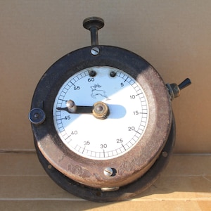 Könnte beinhalten: Ein runder, industrieller Vintage-Timer mit einem dunklen, verwitterten Metallgehäuse und einem weißen Zifferblatt. Das Zifferblatt zeigt schwarze Zahlenmarkierungen von 5 bis 60, einen silbernen Zeiger und eine kleine springende Hirschgrafik.