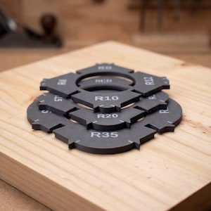 May include: A set of dark grey corner radius templates stacked on top of each other. Each template features white printed text including R5, R10, R15, R20, R25, R30, and R35, indicating specific radius measurements for woodworking and routing tasks.