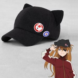 Könnte beinhalten: Schwarze Baseballkappe mit Katzenohren und zwei runden Ansteckern. Die Anstecker sind rot, weiß und blau. Die Kappe hat einen gebogenen Schirm und ist aus weichem Material.