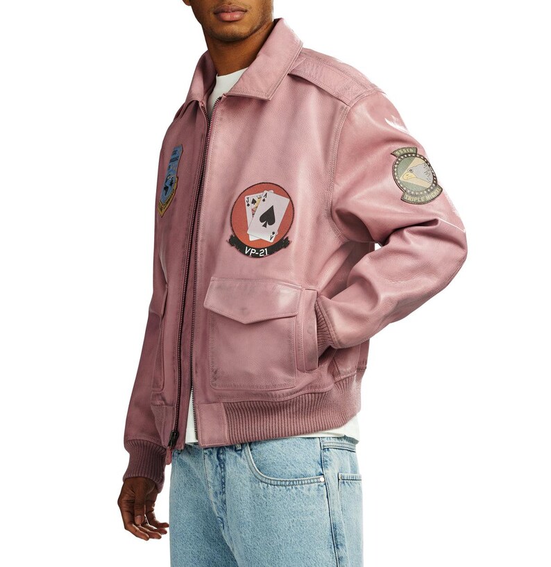 Pu&ograve; includere: Un giubbotto bomber in pelle rosa polvere con colletto classico, polsini e orlo a coste e chiusura frontale con zip. La giacca &egrave; decorata con diverse toppe circolari, tra cui una che mostra carte da gioco e il testo VP-21.