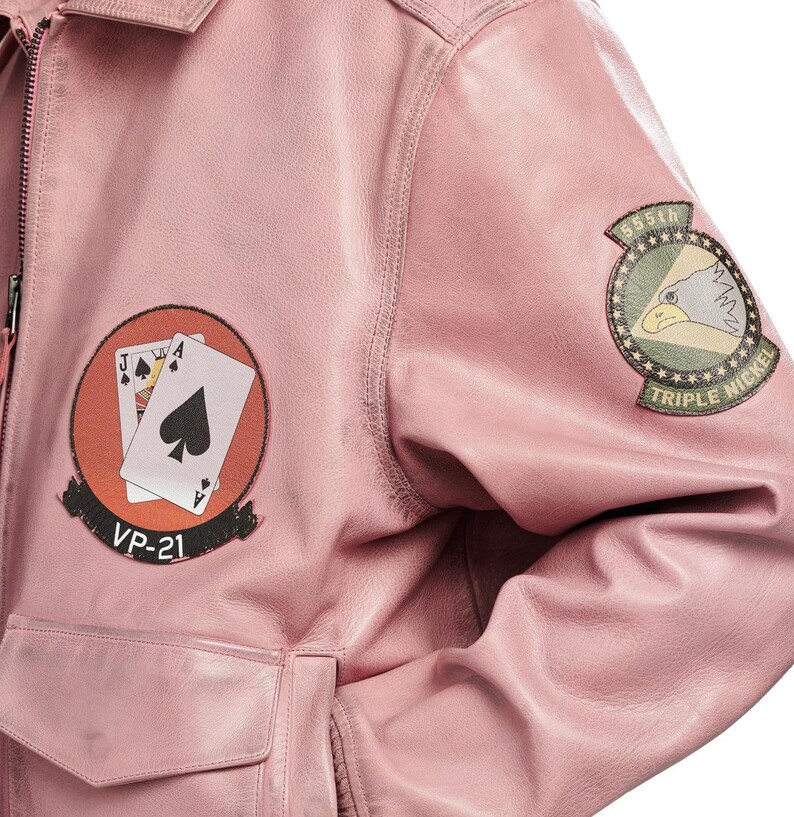 Pu&ograve; includere: Un giubbotto bomber in pelle rosa chiaro con una toppa circolare sul petto raffigurante due carte da gioco e il testo VP-21, e una toppa circolare sulla manica con un'aquila e il testo 555th TRIPLE NICKEL.