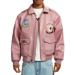 Pu&ograve; includere: Un giubbotto bomber in pelle rosa polvere con cerniera frontale, polsini a coste e due tasche con patta. Il petto presenta toppe ricamate, tra cui un emblema Strategic Reconnaissance Center Avirex Air Command e una grafica di carte da gioco VP-21.